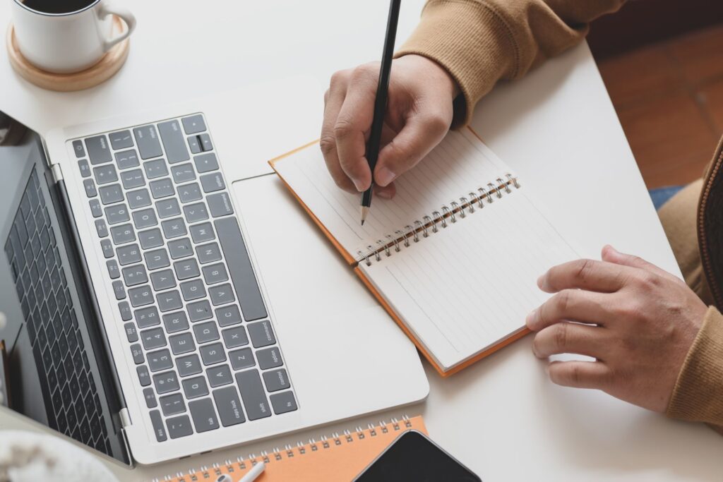 Personne écrivant sur un cahier à côté d'un ordinateur portable durant un webinaire